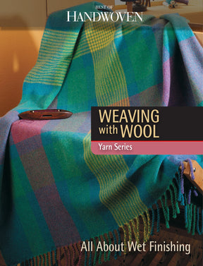 A comfortable wool blanket featuring a striped pattern in blue, green, purple, and yellow is draped over a wooden chair. A small bowl is placed on the blanket. The text reads "Best of Handwoven Yarn Series: Weaving with Wool: All About Wet Finishing" by Long Thread Media.