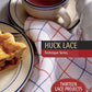 A table setting showcases a slice of pie on a plate, accompanied by a cup of tea and a teapot on a woven cloth adorned with blue and red stripes. This image graces the cover of "Best of Handwoven Technique Series: Huck Lace (Printed Version)" from Long Thread Media, highlighting thirteen lace projects.