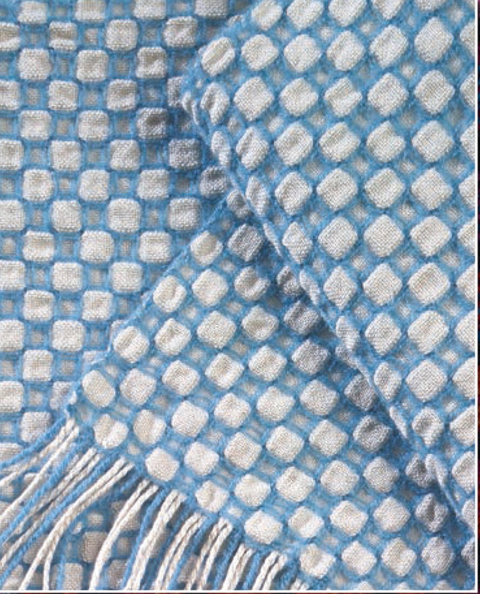 A close-up of the Handwoven's Master Weaver Collection fabric with a grid design. The fabric features soft, rounded white squares inside light blue squares. One edge of the fabric has light blue fringe, hinting that it could be a blanket or scarf from Long Thread Media's collection inspired by Madelyn van der Hoogt's projects and lessons. The texture appears soft and woven.