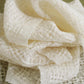 A soft, ivory-colored gauze fabric is loosely folded and layered, showcasing its delicate, open-weave texture. The backdrop of Long Thread Media's Handwoven's Master Weaver Collection: Favorite Projects and Lessons from Madelyn van der Hoogt eBook Printed Copy provides a subtle greenish hue, adding contrast to the light fabric.