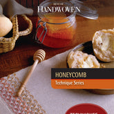 A jar of honey sits next to a honey dipper on a textured cloth, highlighting the intricate beauty of the honeycomb weave. Nearby, a slice of buttered bread peeks out beside another loaf nestled in a woven basket. The accompanying text reads "Best of Handwoven Technique Series: Honeycomb eBook (Printed version)" by Long Thread Media.