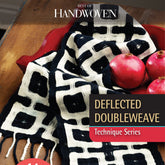 A black and white deflected doubleweave textile with a geometric pattern is draped over a wooden table, showcasing the creativity of contemporary weavers. Two pomegranates rest on the table. Text on the image reads "Best of Handwoven Technique Series: Deflected Double Weave" by Long Thread Media.