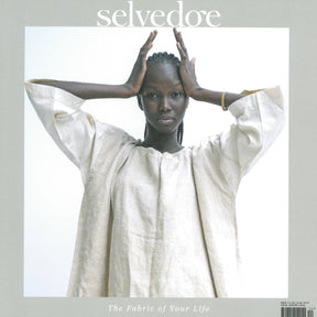 A dark-skinned model wearing a loose, light beige outfit poses with both hands raised and resting on her head. The word "Selvedge" is at the top, and "The Fabric of Your Life" is at the bottom of the image. This edition, titled "Issue 112: Wonder" by Selvedge, highlights sustainable practices rooted in ancestral knowledge against a light grey background.