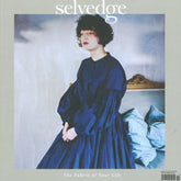 Cover of Selvedge - Issue 119: France. The magazine features a person with curly hair in a loose dark blue dress, sitting on the edge of a bed. The background is set against light-colored walls with folded blue fabrics. The text reads "selvedge" and "The Fabric of Your Life." This issue highlights French slow fashion, blending elegance with sustainability.