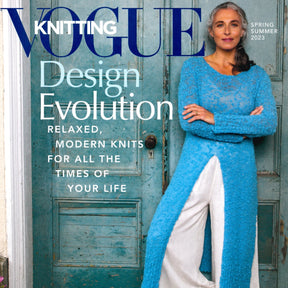 Cover of the Vogue Knitting Spring / Summer 2023 issue by Soho Publishing, showcasing a woman with long, gray hair wearing a blue knit sweater over white pants, leaning against a vintage teal door. The cover text reads "Fiber Journey - Relaxed, Modern Knits For All The Times Of Your Life.