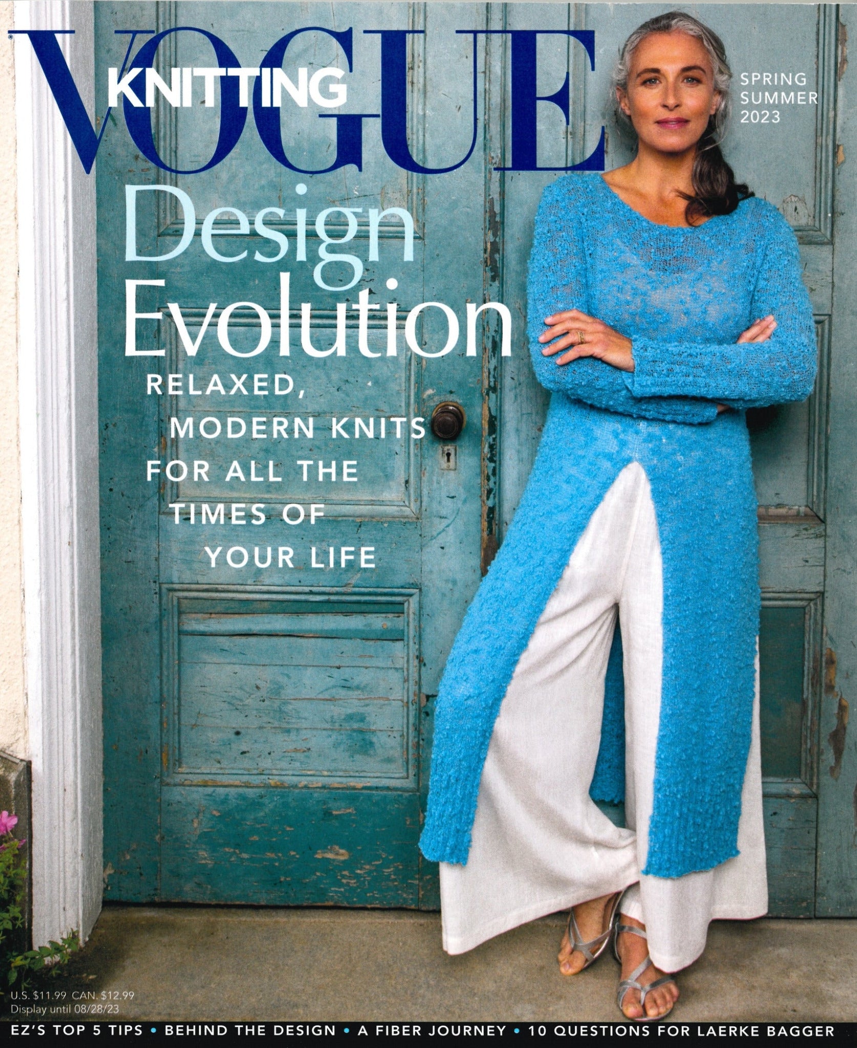 The Vogue Knitting Spring/Summer 2023 issue by Soho Publishing showcases a confident woman with long gray hair clad in a blue knit top and white wide-leg pants, standing against a vintage wooden door. The main headline reads "Design Evolution: Modern Knits for All the Times of Your Life.