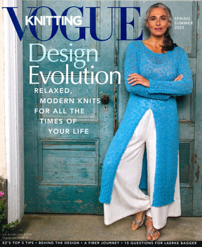 The Vogue Knitting Spring/Summer 2023 issue by Soho Publishing showcases a confident woman with long gray hair clad in a blue knit top and white wide-leg pants, standing against a vintage wooden door. The main headline reads "Design Evolution: Modern Knits for All the Times of Your Life.