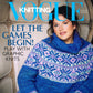 A woman sits on a chair wearing a blue and pink patterned knit sweater, with the cover of Vogue Knitting Winter 2022/23 by Soho Publishing featuring the headline: "Let the games begin! Play with graphic knits." She is surrounded by a warm wooden background as she explores Stitch Cinematique.