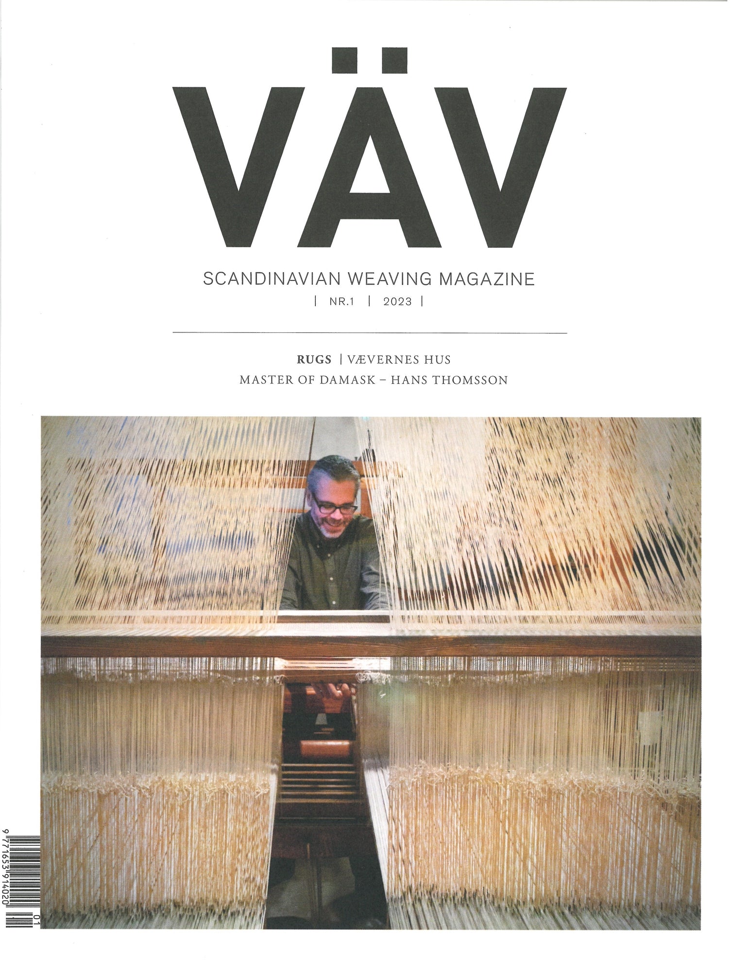 Cover of VÄV Magazine, VÄV Magasinet 1/23. The image depicts a person working at a large weaving loom, surrounded by intricate threads. The text highlights topics such as Viking-Age furnishing textiles and "I Vevernes Hus," and mentions Hans Thomsson, a master of damask.