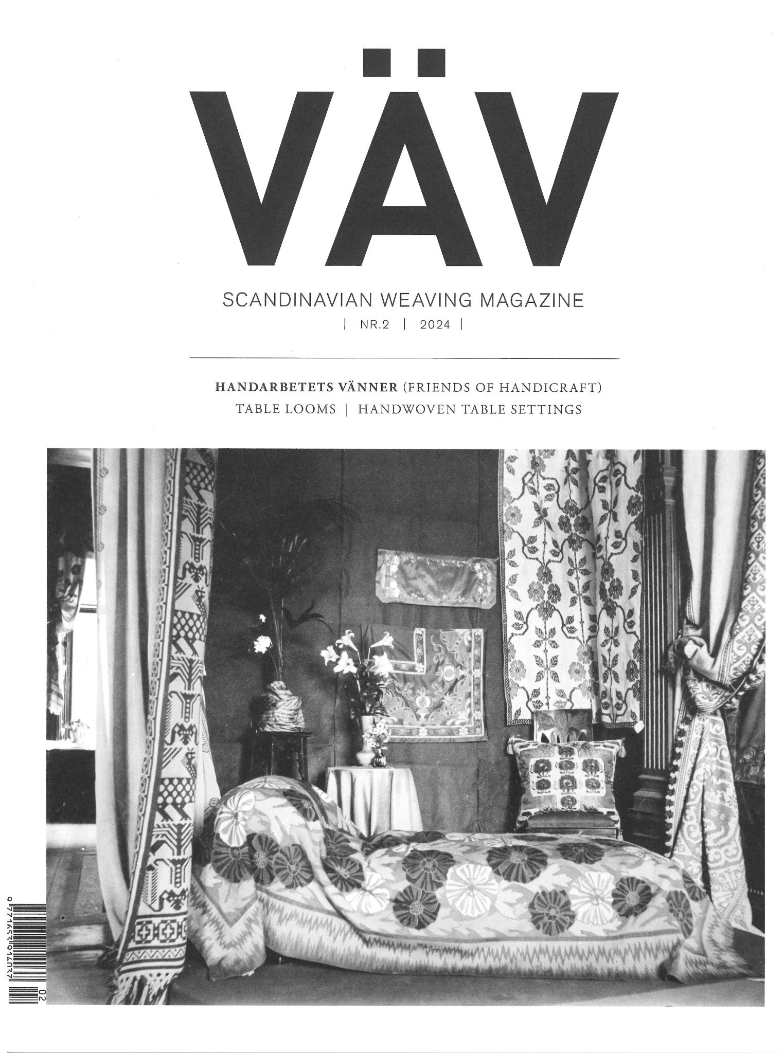 The black and white cover of "VÄV Magasinet 2/24" from VÄV Magazine features an interior adorned with intricate woven textiles, including medieval wool fabrics used in curtains, a bedspread, and cushions. A small table with a flower vase adds to the scene.