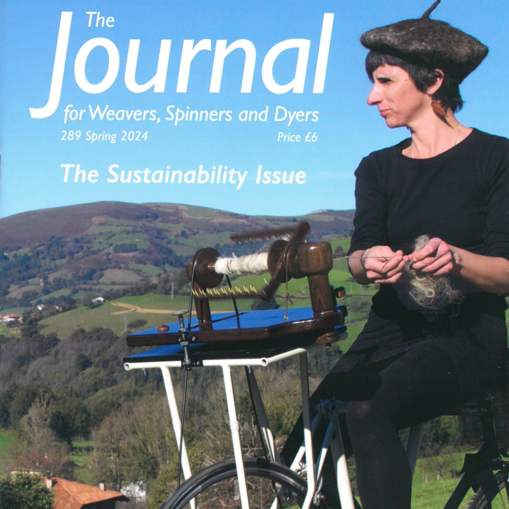 Cover of "The Journal for Weavers, Spinners and Dyers" - UK - Issue 289, Spring 2024. A woman spins yarn on a spinning wheel attached to a stationary bicycle against a background of rolling green hills and distant mountains. The headline reads "The Sustainability Issue: Textiles for Tomorrow.