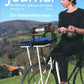 Cover of "The Journal For Weavers, Spinners and Dyers" UK Issue 289, Spring 2024. Features a person in a beret spinning yarn on a bicycle-mounted spinning wheel, set against a countryside landscape. The text reads: "The Sustainability Issue." Learn about our Summer School programs inside.