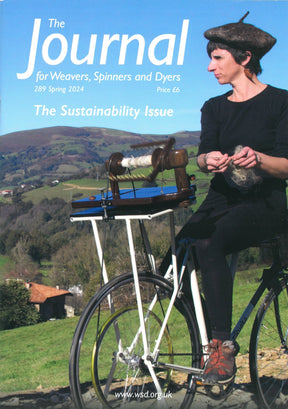 Cover of "The Journal For Weavers, Spinners and Dyers" UK Issue 289, Spring 2024. Features a person in a beret spinning yarn on a bicycle-mounted spinning wheel, set against a countryside landscape. The text reads: "The Sustainability Issue." Learn about our Summer School programs inside.