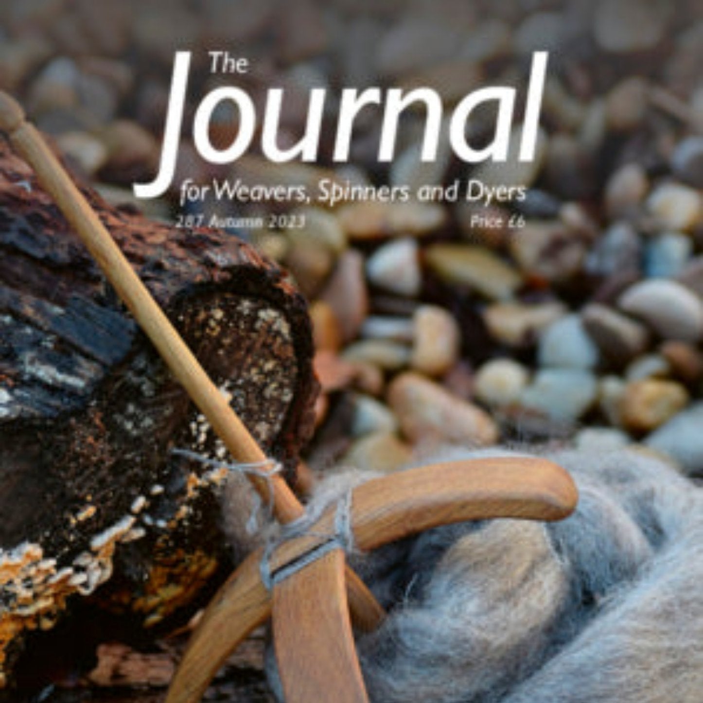 A spindle and gray wool roving are displayed on a textured background of pebbles and logs, highlighting the craft of dyeing. The latest issue of "The Journal For Weavers, Spinners and Dyers" showcases this artwork prominently at the top, marked as "287 Autumn 2023," with a price of £6, celebrating the intricate realm of textile design.