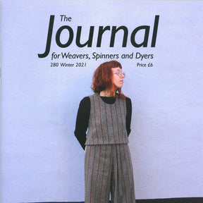 A red-haired woman wearing a gray sleeveless top over a black shirt and matching pants stands against a plain white wall, looking to the right. The text above her reads: "The Journal For Weavers, Spinners and Dyers - UK - Issue 280, Winter 2021," which explores natural dyes in modern cloth production.