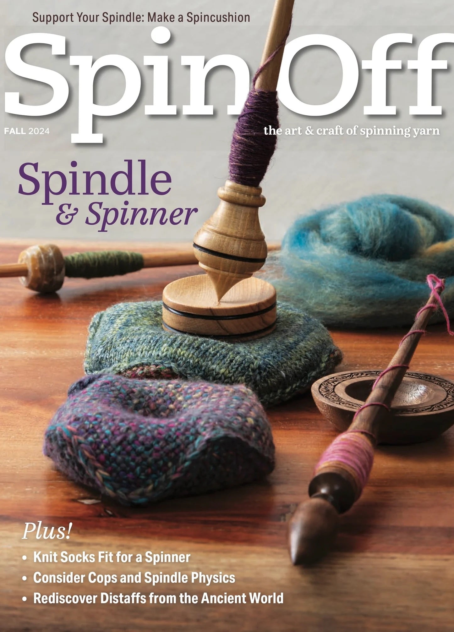 The cover of "Spin Off Fall 2024" by Long Thread Media showcases a wooden spindle adorned with handspun yarn resting on a textured mat. Additional spindles and components are visible in the background, with text promoting articles about the physics of supported spindles, the use of distaffs, and knitting socks tailored for spinners.