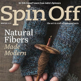 Cover of Long Thread Media's "Spin Off Winter 2025" magazine. It showcases an individual wearing knitted gloves, grasping a spindle with handspun brown yarn. The cover text emphasizes "Natural Fibers Made Modern" and features an article on Eri Silk Cakes along with the allure of textured yarn in modern designs.