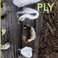 White and black curly fiber strands are artfully arranged on a weathered wooden surface for the cover of PLY Magazine's The Science Issue, Spring 2023, highlighting sustainable approaches in handspinning and fiber preparation.