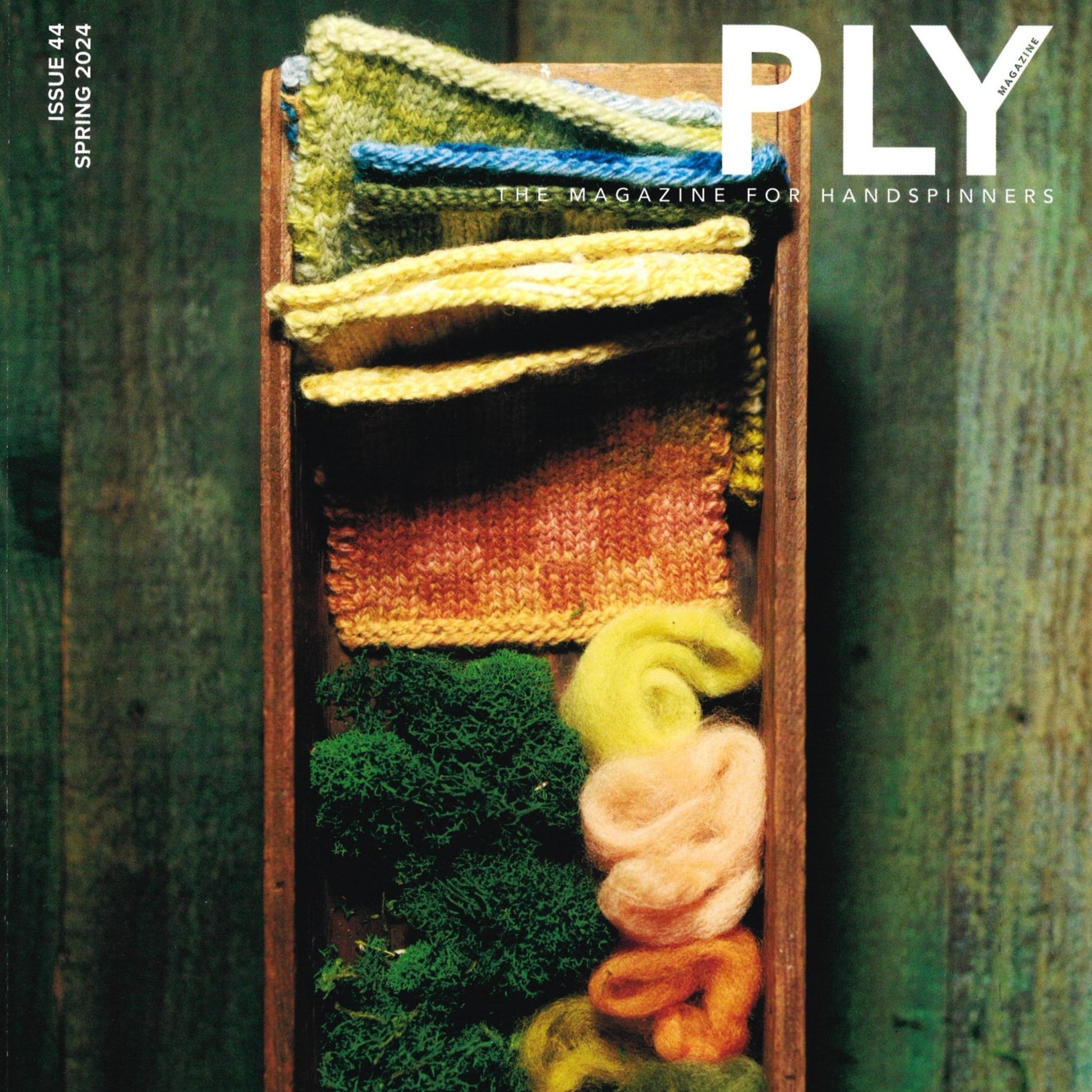 A wooden box filled with various knitted fabric swatches in green, yellow, and orange hues, accompanied by bundles of matching colored wool roving and green moss, is featured on the cover of "PLY - The Magazine for Handspinners," Issue 44, Spring 2024: Growth. This issue from PLY Magazine highlights yarn structure and spinning skills.