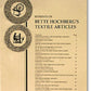 The cover page of a document titled "Bette Hochberg’s Textile Articles" by Foxglove Fiberarts Supply features an index listing various articles with corresponding page numbers. The cover also includes illustrations of a spinning wheel and a person weaving handwoven textiles, flanking the title text on either side.