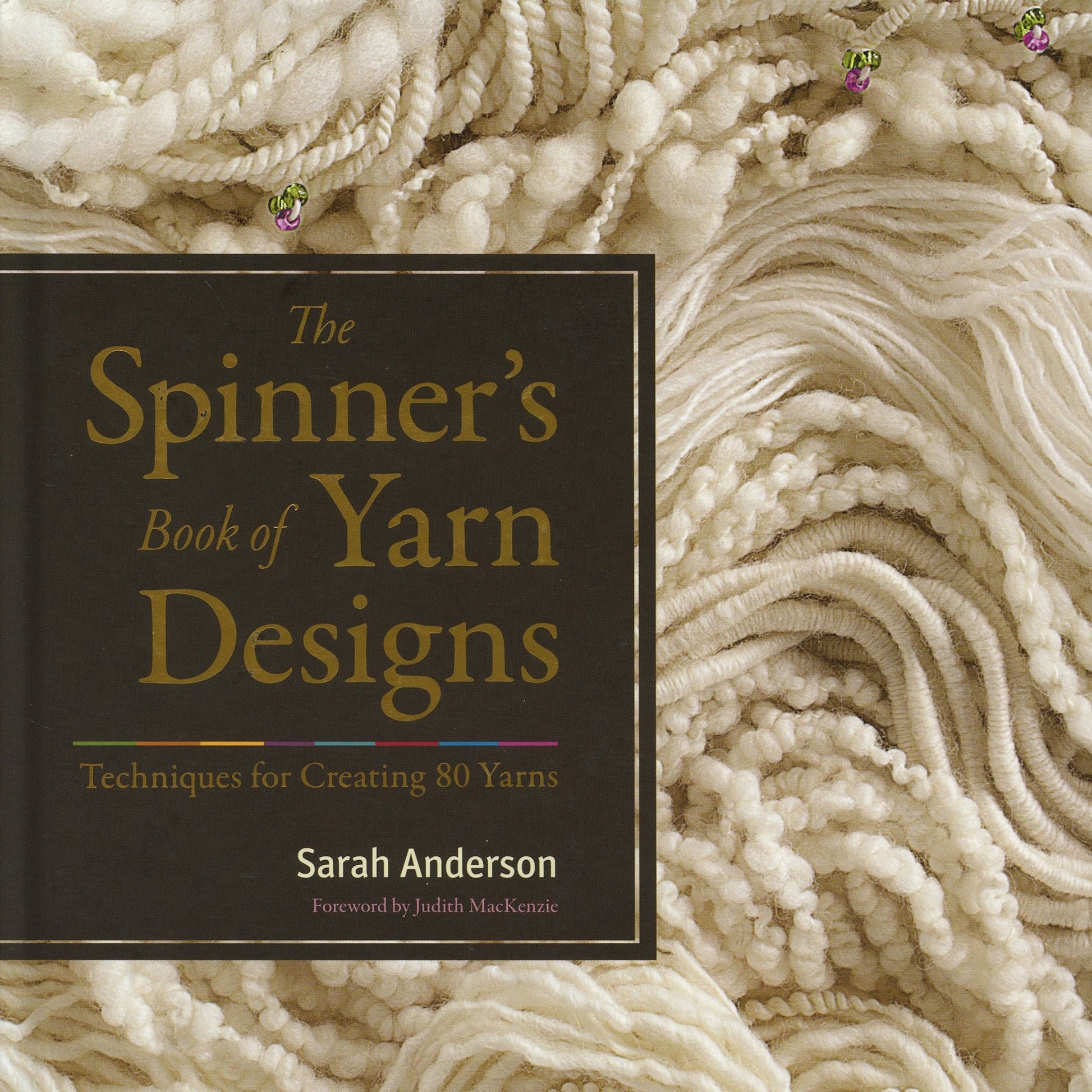 The cover image of "The Spinners Book of Yarn Designs: Techniques for Creating 80 Yarns" by Sarah Anderson, from Ingram Content, featuring a foreword by Judith MacKenzie. The background showcases an array of white and cream yarn textures, highlighting the art of spinning yarn. The text is displayed in a bold, elegant font.