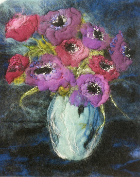 The "Art in Felt & Stitch" by Ingram Content showcases a vibrant mixed-media artwork featuring a bouquet of intricately detailed purple and pink flowers crafted through needle felting. The flowers, with their green stems, are arranged in a textured, light blue vase set against a deep blue and black background. This piece exemplifies the artist's skillful use of color and texture.