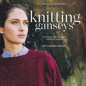 Close-up of a woman wearing a burgundy knitted sweater, looking contemplatively into the distance. The image is the cover of "Knitting Ganseys - Revised and Updated" by Ingram Content, authored by Beth Brown-Reinsel.