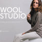 A woman sits on a white surface, wearing a gray cable-knit sweater and light-colored pants. The text “Wool Studio: The knit.wear Capsule Collection” by Ingram Content is displayed, highlighting the luxurious knitwear designs with "Meghan Babin" mentioned in smaller text at the bottom.