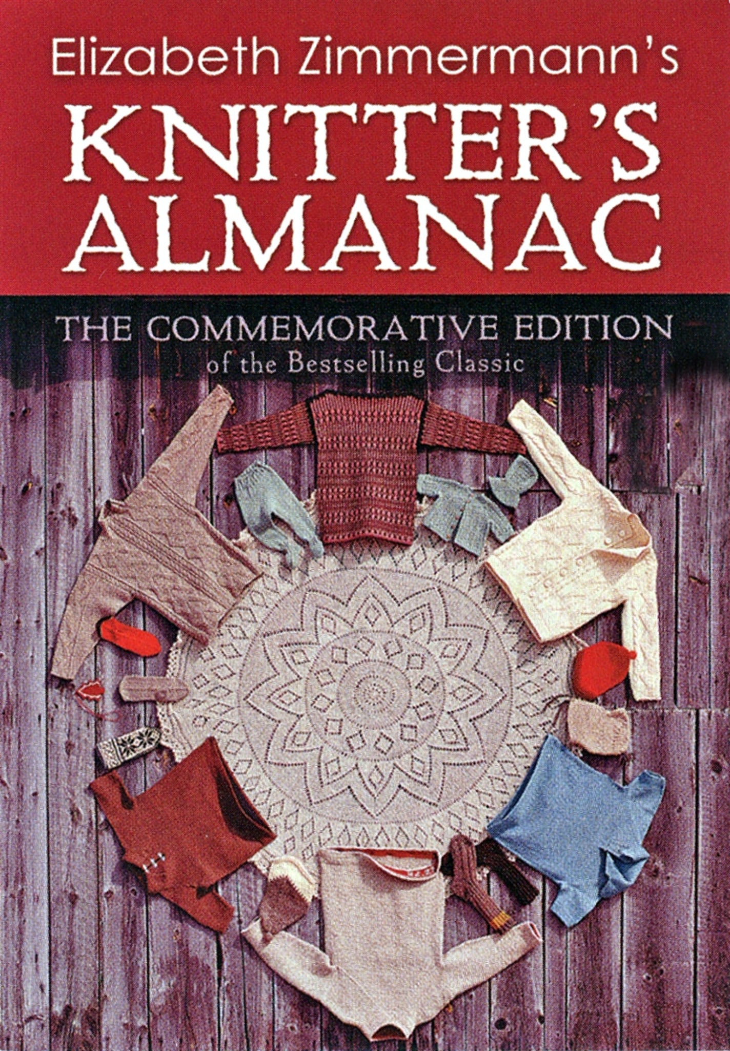 Cover of the book "Elizabeth Zimmermann's Knitter's Almanac - Commemorative Edition" by Dover Books. The image features various knitted sweaters and garments arranged in a circle around a knitted doily on a wooden background. Ideal for intermediate knitters, the title is in white text on a red background.