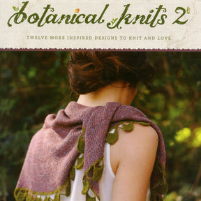 The cover of "Botanical Knits 2" by Never Not Knitting features a person with their back to the viewer, adorned in a purple knitted shawl accented with green, leaf-like details. The title and subtitle read, "Botanical Knits 2: Twelve More Inspired Designs to Knit and Love." A scenic forest background can be seen.