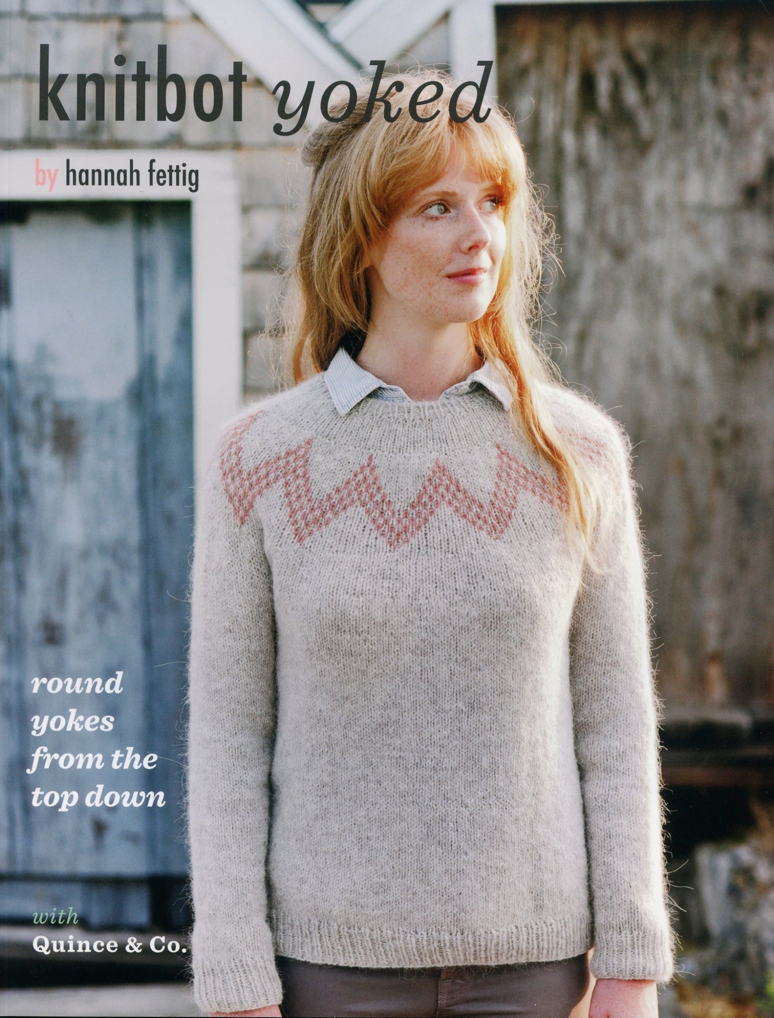 A person with long hair stands outside wearing a light-colored round-yoke sweater featuring a zigzag pattern around the yoke and a subtle pink design. Behind them, there is a rustic building with wooden siding. The text on the image reads: "Knitbot Yoked by Never Not Knitting; round yokes from the top down with Quince & Co.