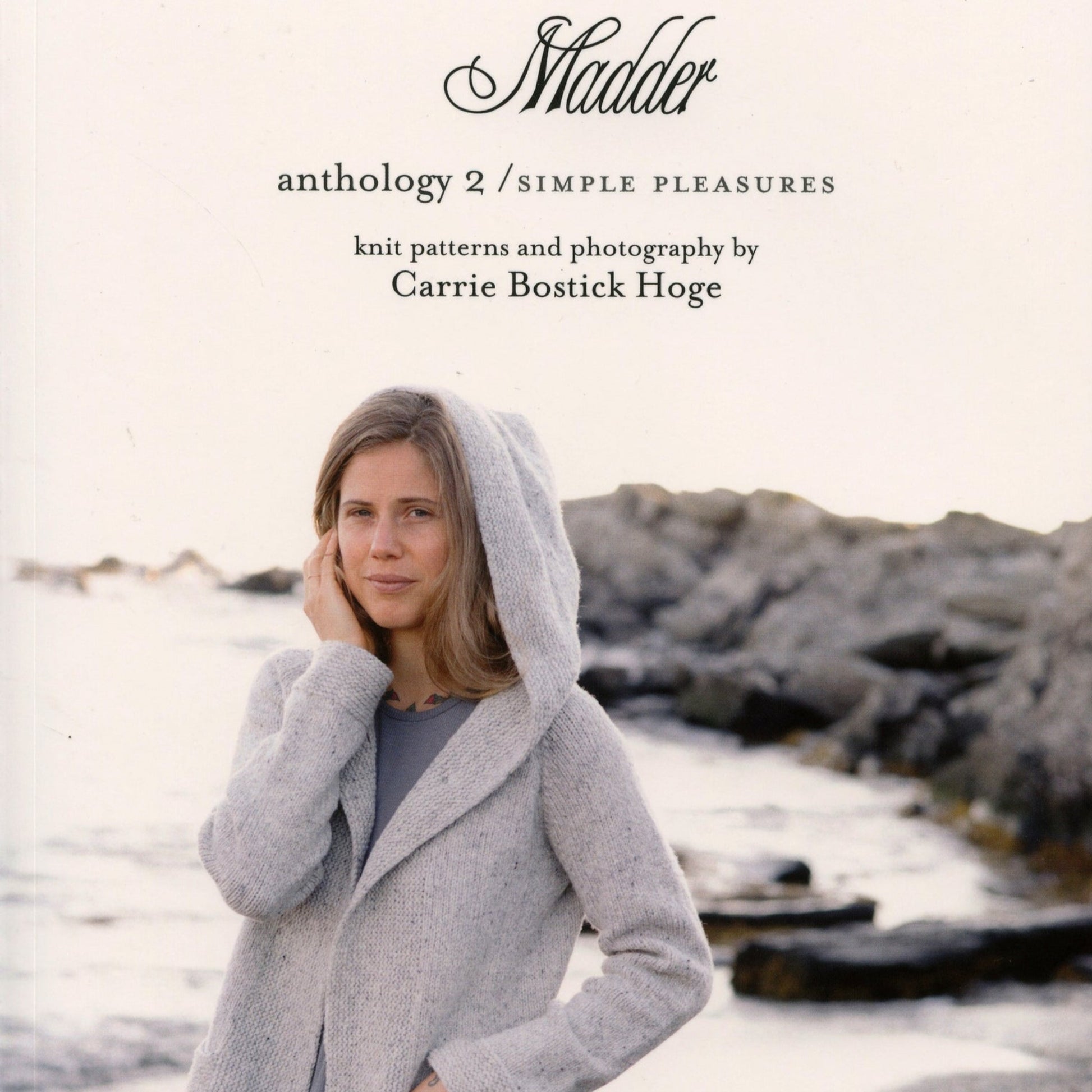 A book cover titled "Madder - Anthology 2 / Simple Pleasures" under the brand Never Not Knitting, featuring a woman standing by a rocky shore, wearing a light gray knitted jacket with a hood. The book contains knitting patterns for sweaters and accessories, complemented by photography from Carrie Bostick Hoge.