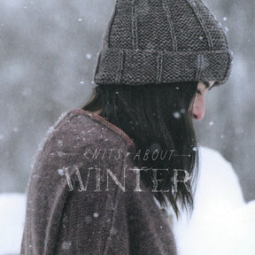 A person in a knitted hat and sweater stands in the snow with their head bowed. Snowflakes are falling gently around them. The text "Knits About Winter by Pom Pom Publishing" is overlaid on the image. The background is a blurred snowy landscape.