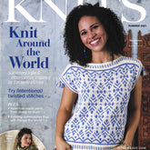 A woman with curly hair smiles, wearing a blue and white knitted top featuring intricate patterns, as she graces the cover of "Interweave Knits Summer 2021" by Golden Peak Media. The magazine explores "Knit Around the World," showcasing knitting projects and designs inspired by global influences.