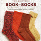 Cover of the book "The Knitter's Book of Socks" by Ingram Content. The image displays four brightly colored knitted socks in shades of red, multicolored, orange, and yellow, carefully laid out in a row on a textured white backdrop. The subtitle announces "The Yarn Lover's Ultimate Guide to Creating Socks with Beautiful Sock Patterns.