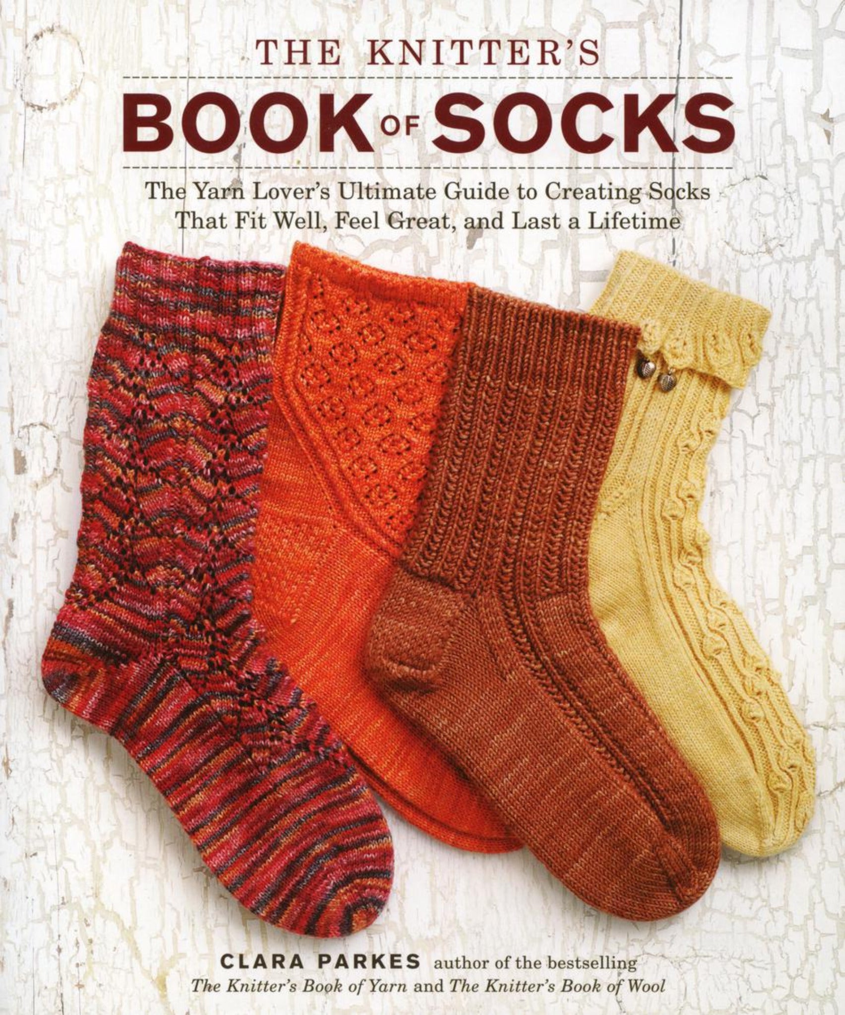 Cover of "The Knitter's Book of Socks" by Clara Parkes, an Ingram Content product, showcasing four intricately knitted socks in shades of red, orange, yellow, and brown set against a textured white background. The subtitle reads: "The Yarn Lover's Ultimate Guide to Creating Socks That Fit Well, Feel Great, and Last a Lifetime," making it an ideal resource for knitting enthusiasts.