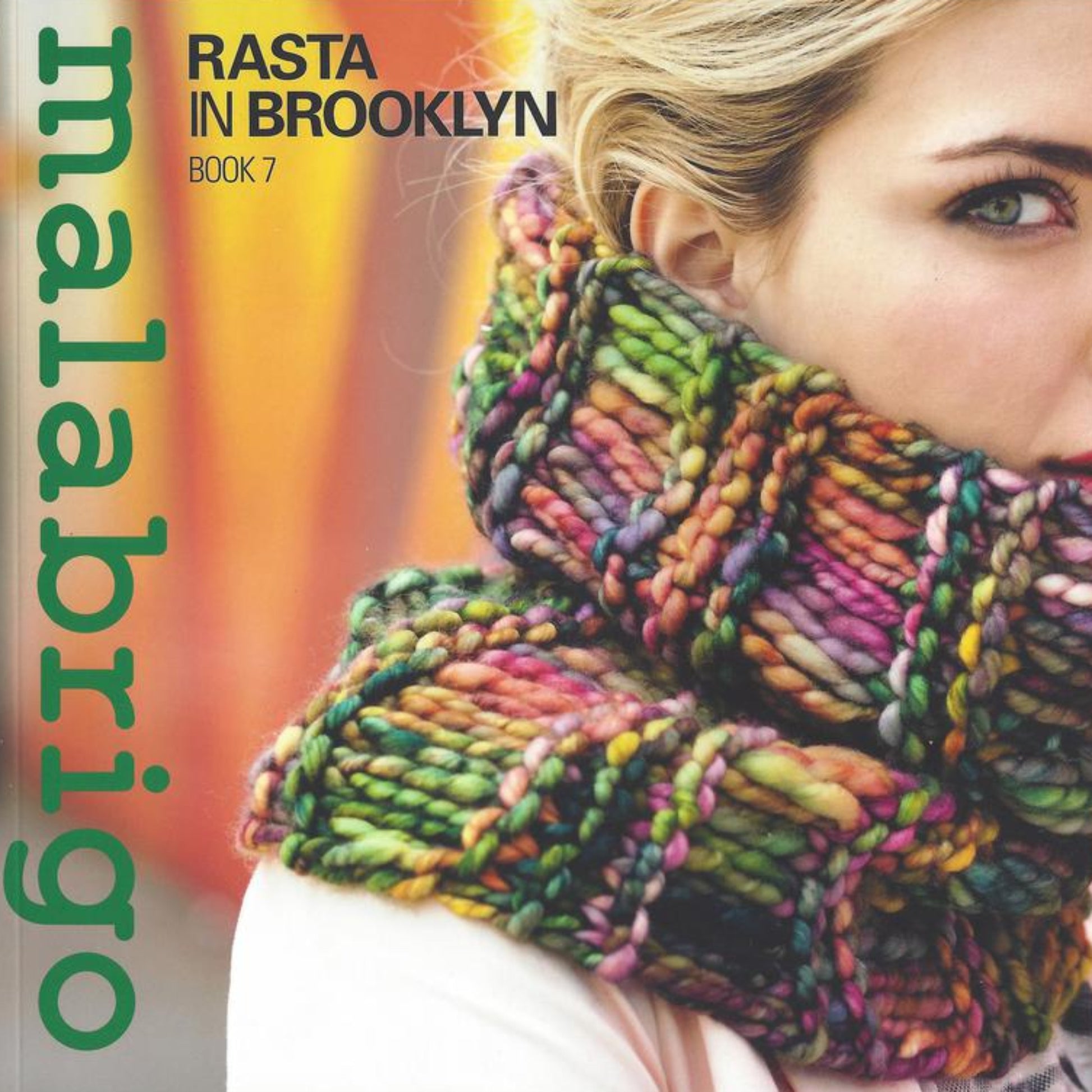 A close-up of a woman wearing a thick, multi-colored knitted scarf covering her mouth. The text on the image reads "Malabrigo Book 7 - In Brooklyn, Rasta" and "Malabrigo Yarn," with the latter running vertically along the left side. Crafted from Malabrigo Rasta yarn, the background is blurred with warm tones.