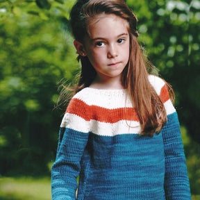 A young girl stands outdoors with a calm expression. She has long brown hair and is wearing a knitted sweater with wide stripes in blue, white, and orange—a design inspired by the unique patterns for kids found in Malabrigo Yarn's Malabrigo Book 9 - Niños. The background is filled with lush green foliage.