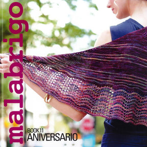 A person wearing a blue top is showcasing a knitted shawl featuring a vibrant pattern in shades of purple, pink, and blue. The text on the image reads "Malabrigo Yarn" on the left side in large pink letters and "Malabrigo Book 11 - Aniversario" at the bottom.