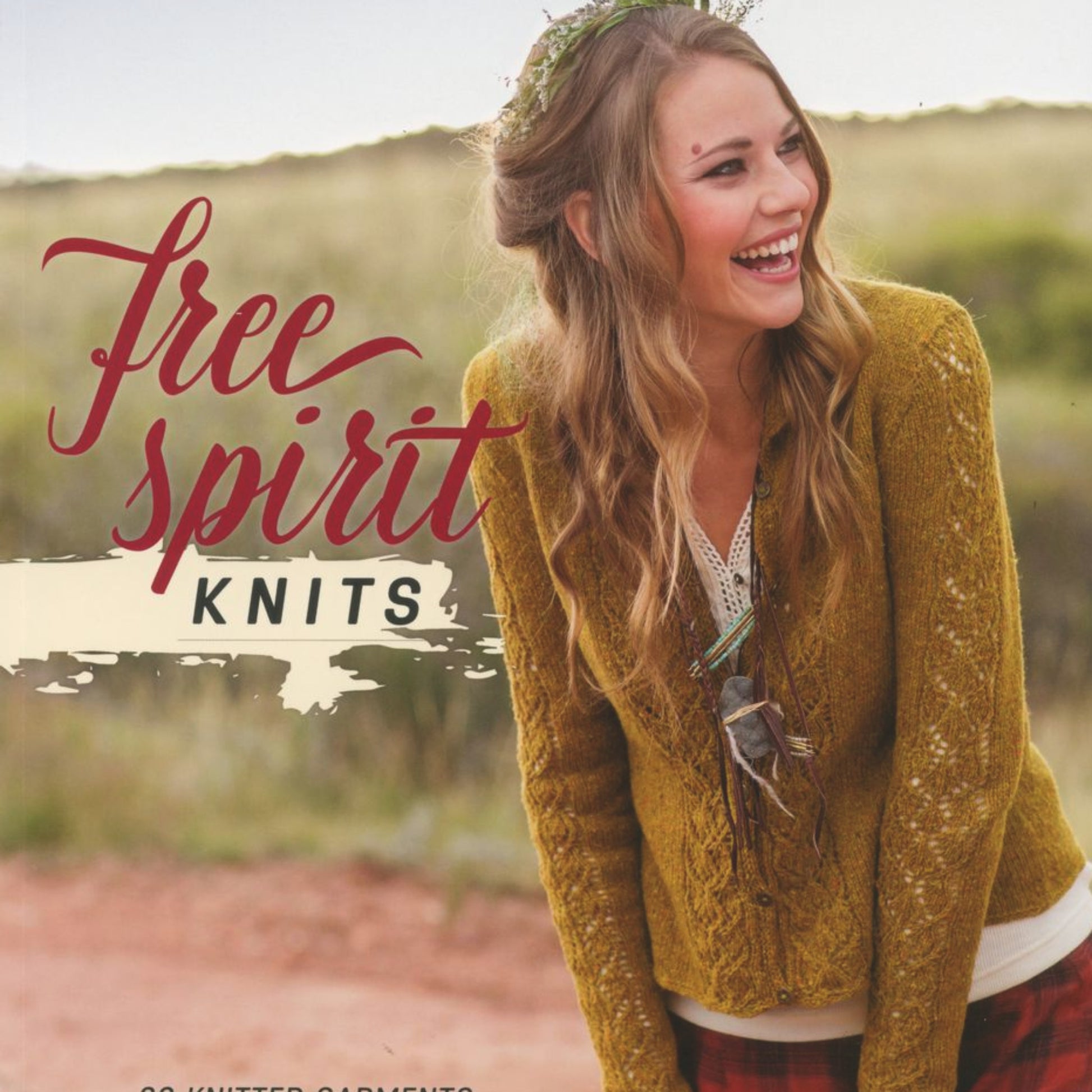 A young woman with long, wavy hair wears a mustard yellow knitted cardigan over a patterned shirt and plaid skirt. She stands outside, smiling and laughing. The text "Free Spirit Knits" by Ingram Content is written in large cursive, with a subtitle indicating knitted garments for knitters of every skill level.