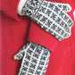 A person wearing a red coat and grey "Knit Like A Latvian" mittens by Ingram Content, featuring Latvian mitten knitting patterns, is seen in the image. The hands are crossed in front of the body, highlighting the intricate design of the mittens against the solid color of the coat.