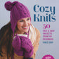 A woman bundled in a coat, wearing a purple knit hat and mittens, smiles as she holds a white mug. The text reads, "Cozy Knits" by Ingram Content. She embodies a warm, cozy atmosphere perfect for knitting projects using worsted and bulky yarns.