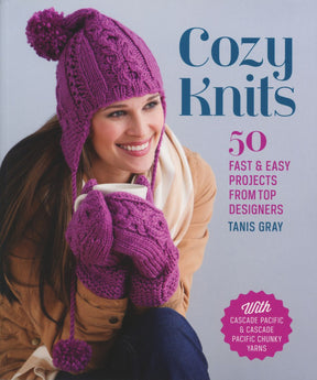 A woman wearing a pink woolen hat and mittens smiles on the cover of "Cozy Knits" by Tanis Gray. A pink badge highlights that the book includes projects featuring Cascade Pacific and Cascade Pacific Chunky yarns, showcasing cozy hats, scarves, and more. This delightful offering is brought to you by Ingram Content.