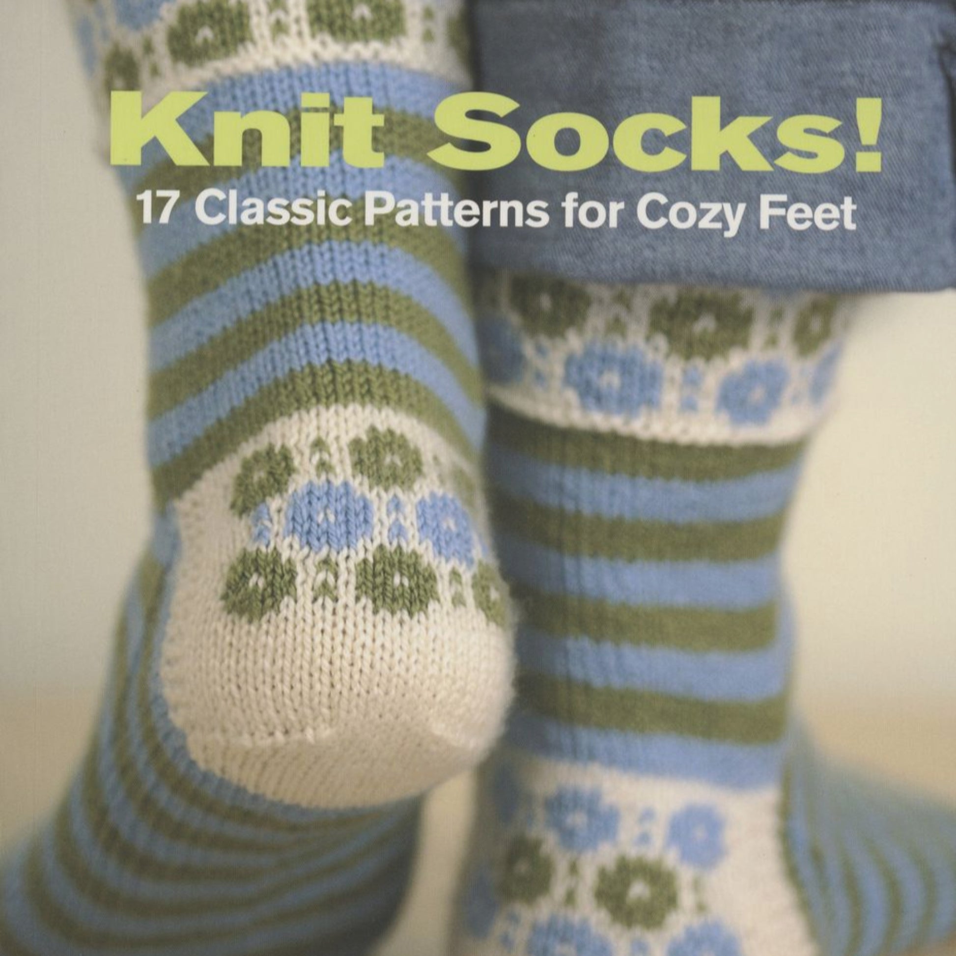 Cover of a book titled "Knit Socks! 17 Classic Patterns for Cozy Feet" by Ingram Content. The image showcases two pairs of feet adorned in colorful knitted socks with blue, green, and white stripes as well as floral patterns. Perfect for any knitting instructor, the feet are crossed against a light background.