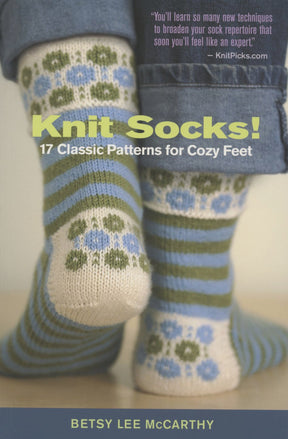 Two feet are adorned with colorful, hand-knit socks displaying floral and striped patterns in green, blue, and white. The socks are prominently featured on the cover of Ingram Content's "Knit Socks! 17 Classic Patterns for Cozy Feet" by knitting instructor Betsy Lee McCarthy.