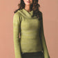 A woman with long, wavy hair is wearing the No-Sew Knits light green, long-sleeved sweater by Ingram Content, featuring a unique collar that drapes loosely. Demonstrating trendy styling, she stands against a plain, muted beige background, looking slightly off to the side with a calm expression.