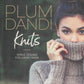 Close-up of a woman partially covering her face with the collar of a chunky knitted sweater. The text at the top reads "Plum Dandi Knits," with the subtitle "Simple Designs for Luxury Yarns" below. The background, filled with natural textures, enhances the luxurious knits on display. Brought to you by Ingram Content.