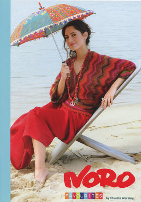 A woman on a sandy beach sits on a wooden chair, holding a colorful parasol. She wears a red zigzag-patterned sweater and a long red skirt made from Noro Taiyo Sock Yarn, accessorized with a peace sign necklace. The text "Noro Favourites by Knitting Fever / Euro Yarns" is at the bottom of the image.