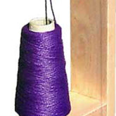 A Leclerc Doubling Stand from Leclerc Looms stands vertically on a wooden surface. Positioned near a vertical wooden panel, the stand features tightly wound vibrant purple thread with its end partially visible at the top, making it perfect for twisting yarns or weaving intricate designs.