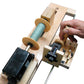 A close-up of the Leclerc Double-Ended Electric Bobbin Winder by Leclerc Looms, showcasing spools of green thread. A person adjusts a knob with their right hand. The device features a counter display and various visible mechanical components, including a black motor and metal rods.